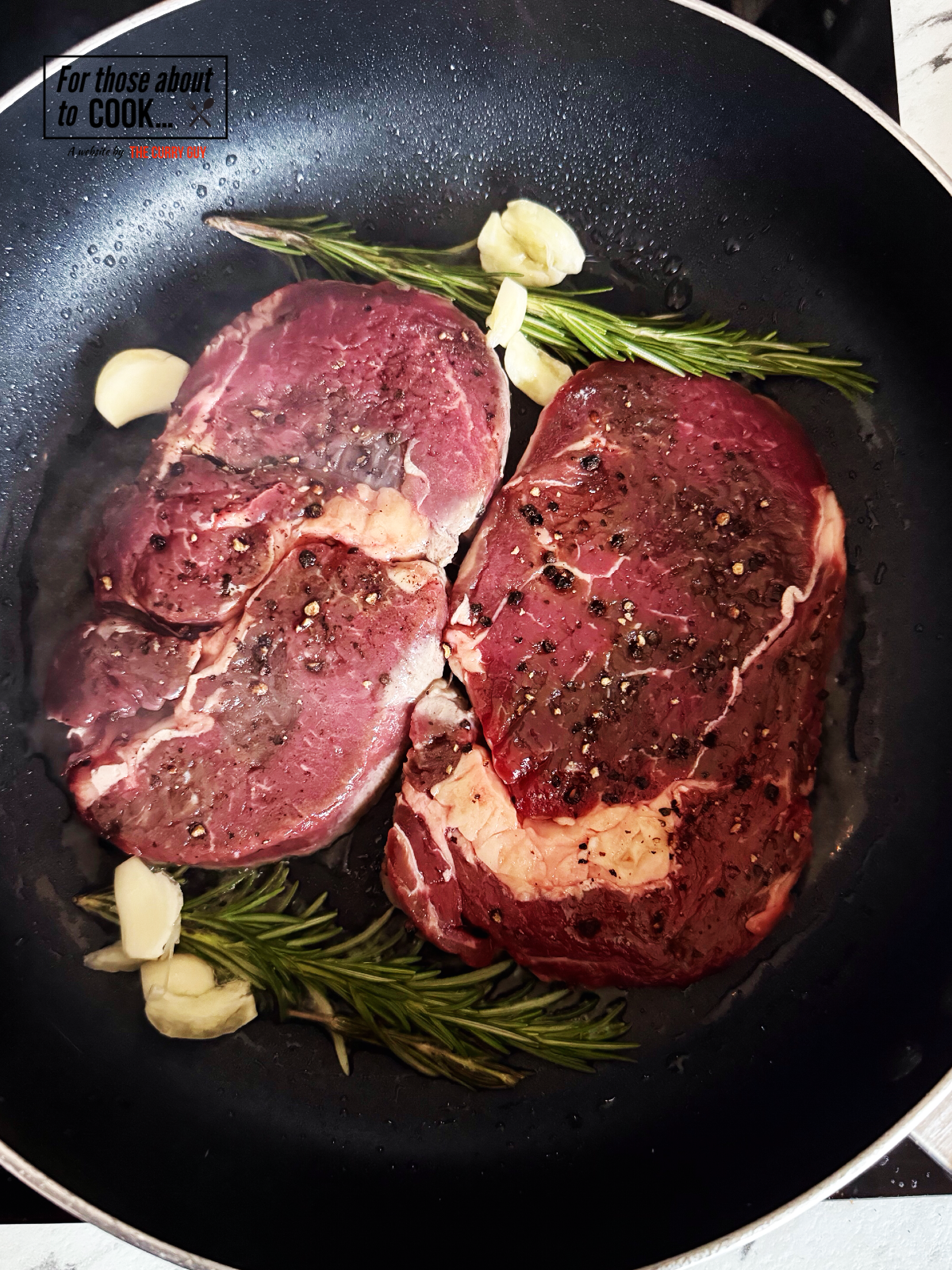 Ribeye steaks frying in a pan with garlic and rosemary