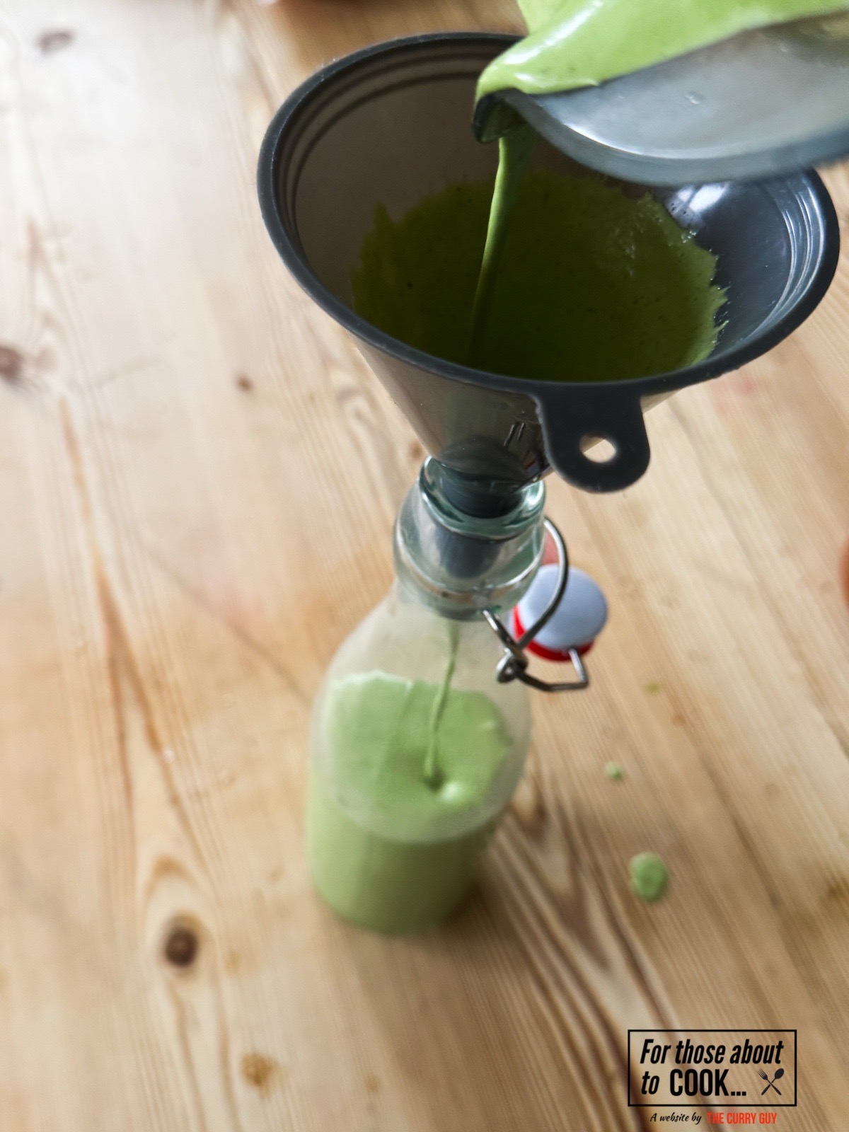 Pouring the green goddess salad dressing through a funnel into a bottle.