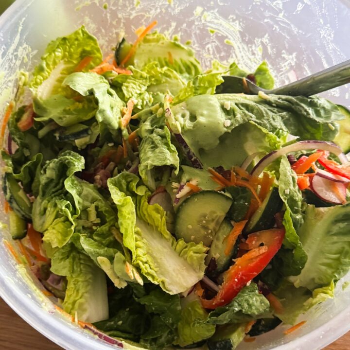 Green goddess dressing tossed into salad vegetables.