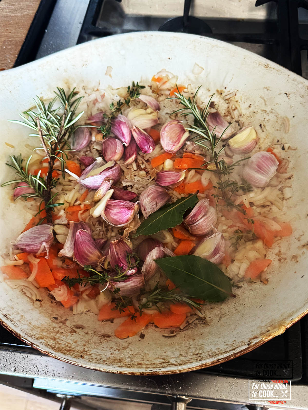 Stirring the garlic cloves and herbs into the onion and carrot mixture in the pan.