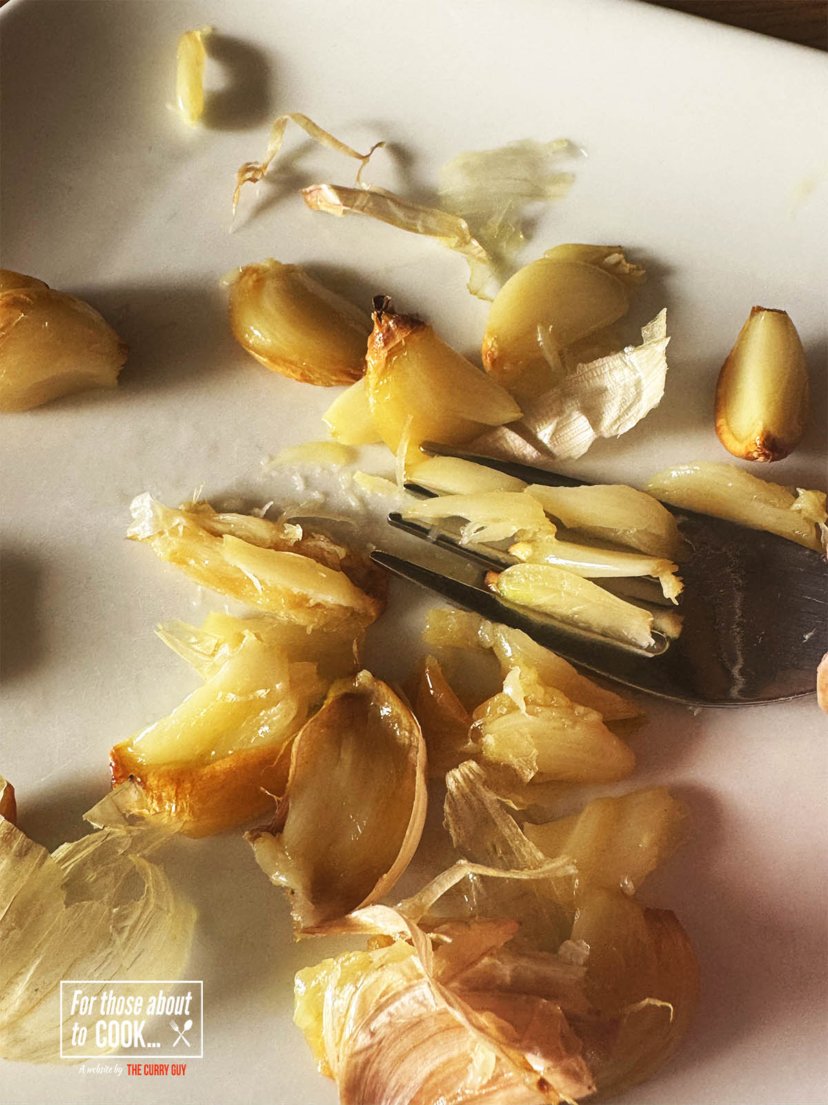 Smashing the roasted garlic before adding it to the pan.