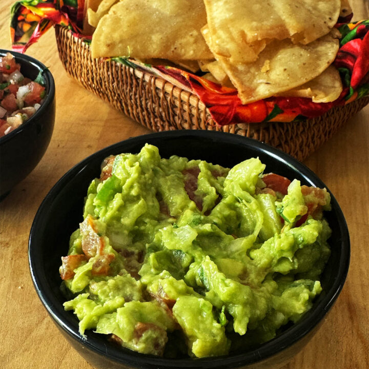 Homemade Guacamole in a serving bowl next to corn chips.