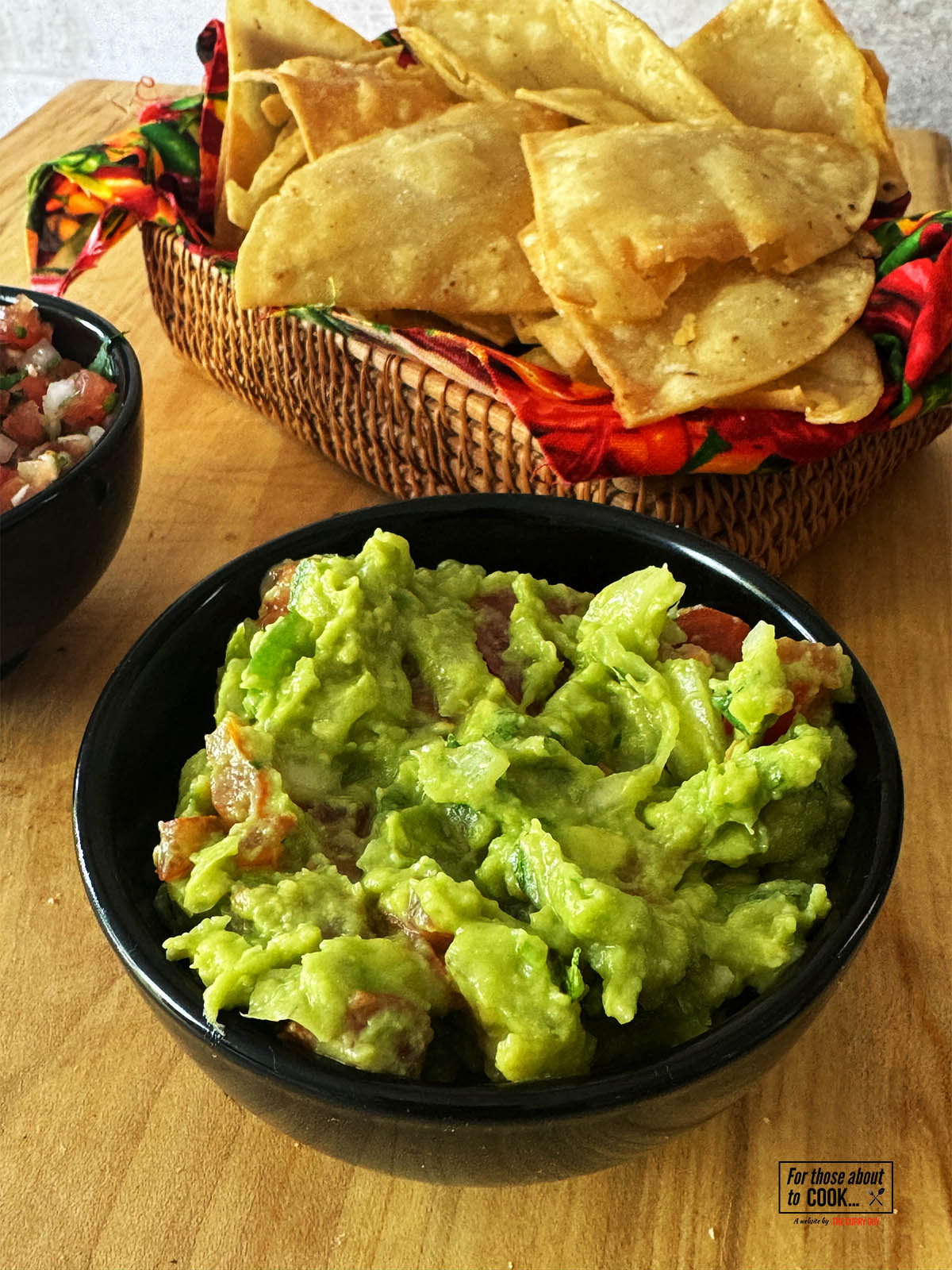 Homemade Guacamole in a serving bowl next to corn chips.