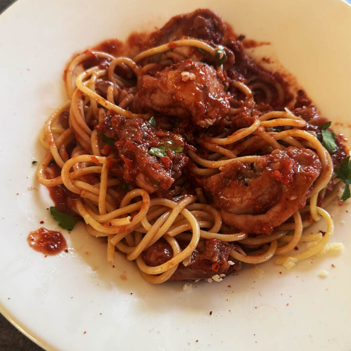 Roman chicken over spaghetti, garnished with parsley and dried chili flakes.