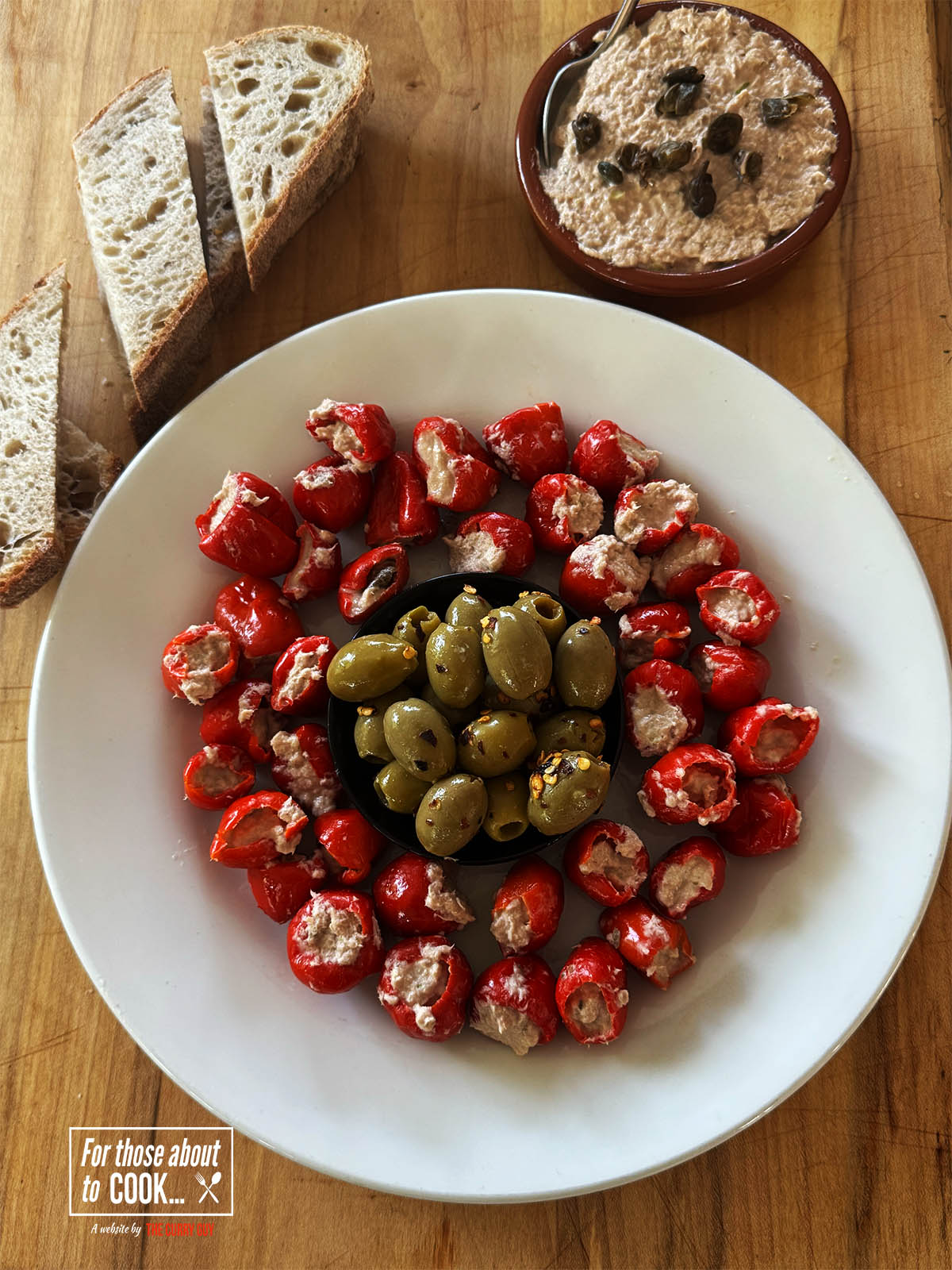 Tuna stuffed peppers on a serving plate with olives, next to bread.