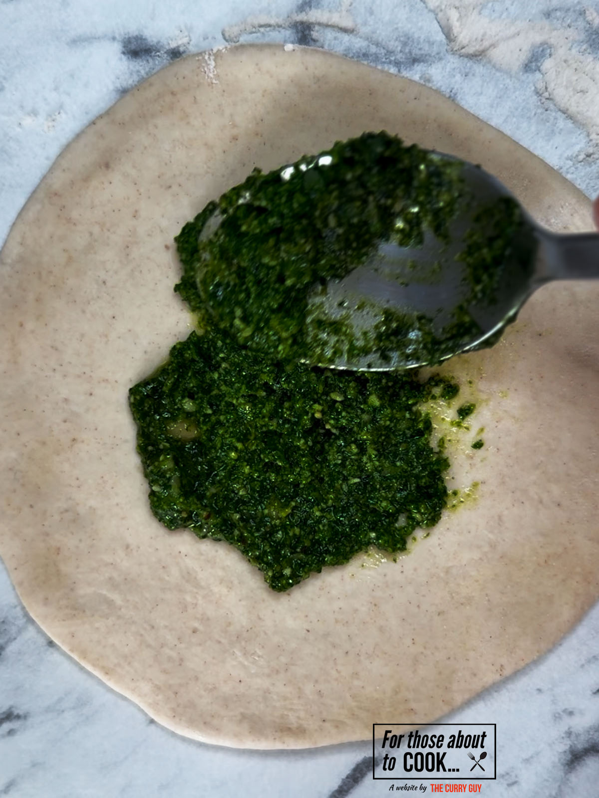 dough flattened and smothered in pesto