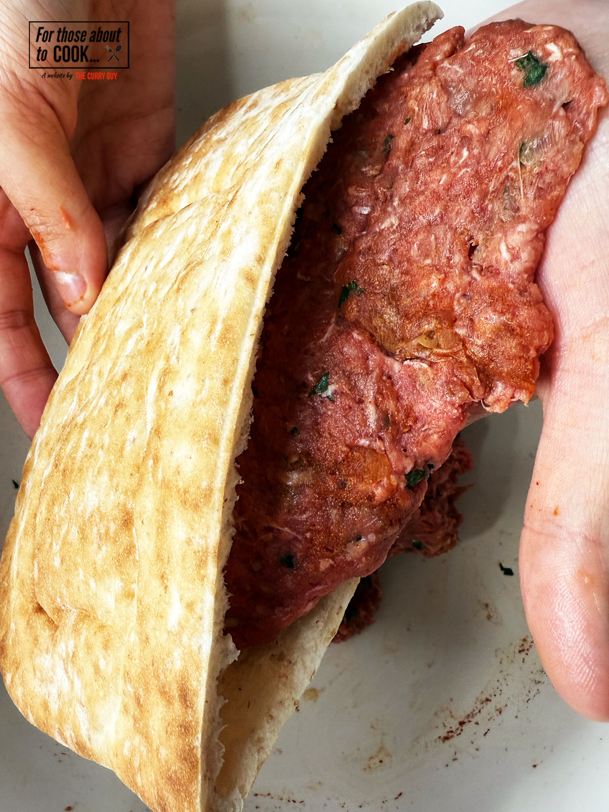 Meat patted into a patty shape being placed in the pita