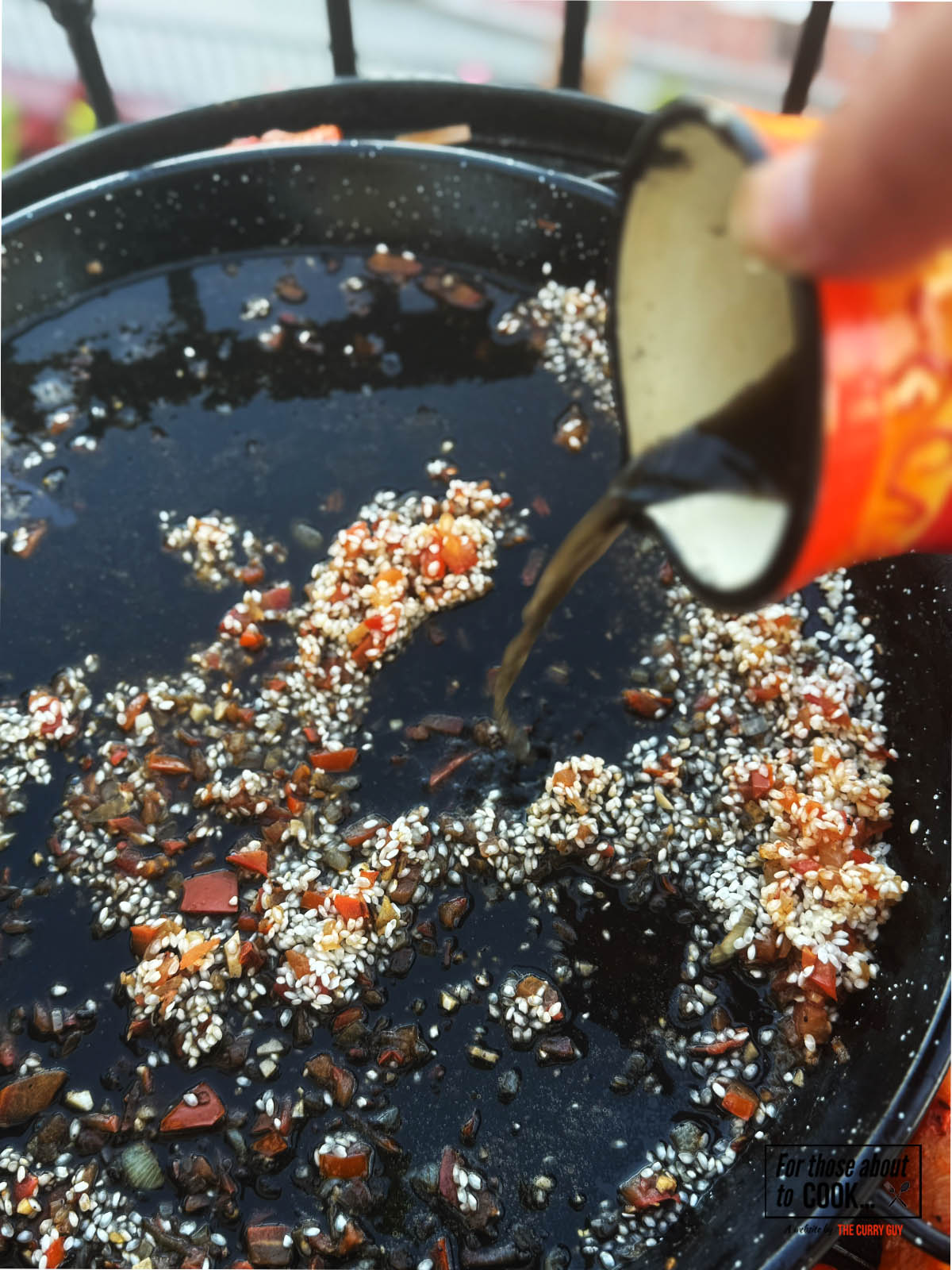 Pouring the seafood stock and squid ink mixture over the rice in the pan.