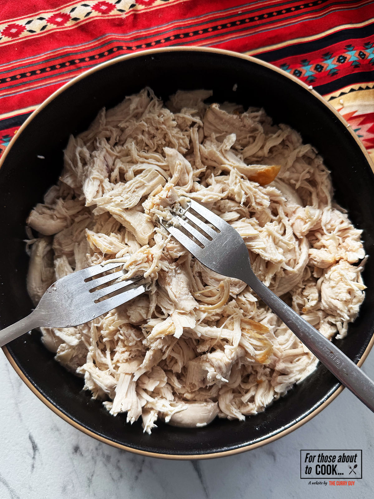 Chicken shredded in a bowl using forks
