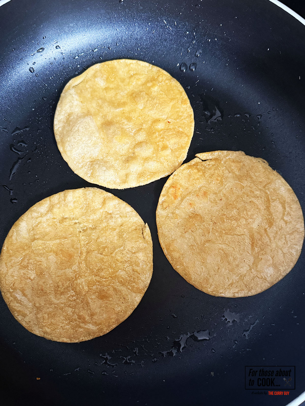 Corn tortillas frying in a pan until crispy