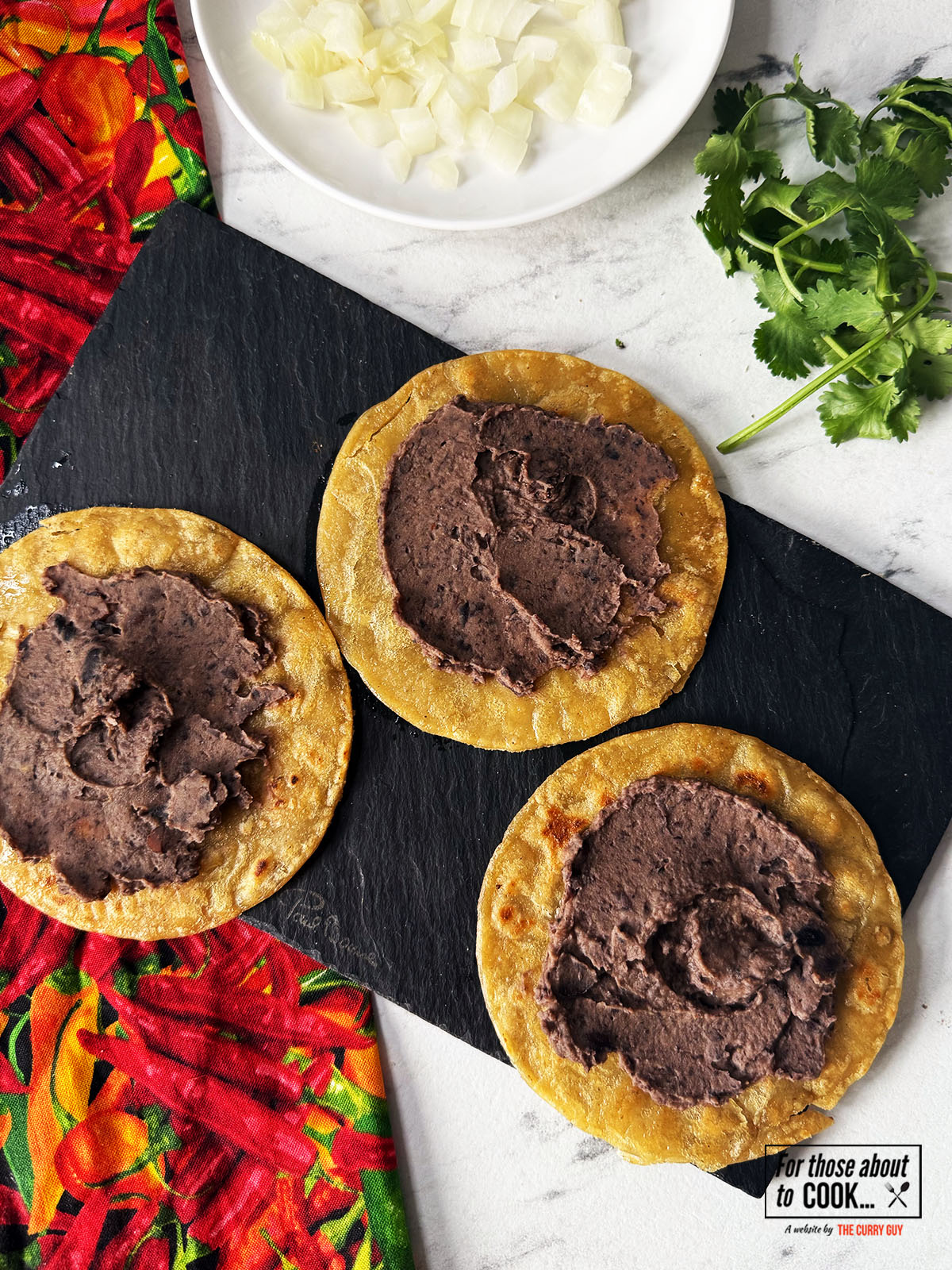 Refried black beans spooned onto fried corn tortillas