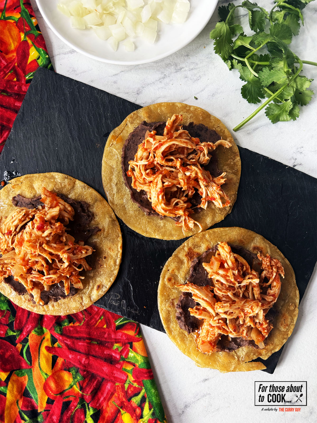 Tinga added on top of black beans on corn tortillas