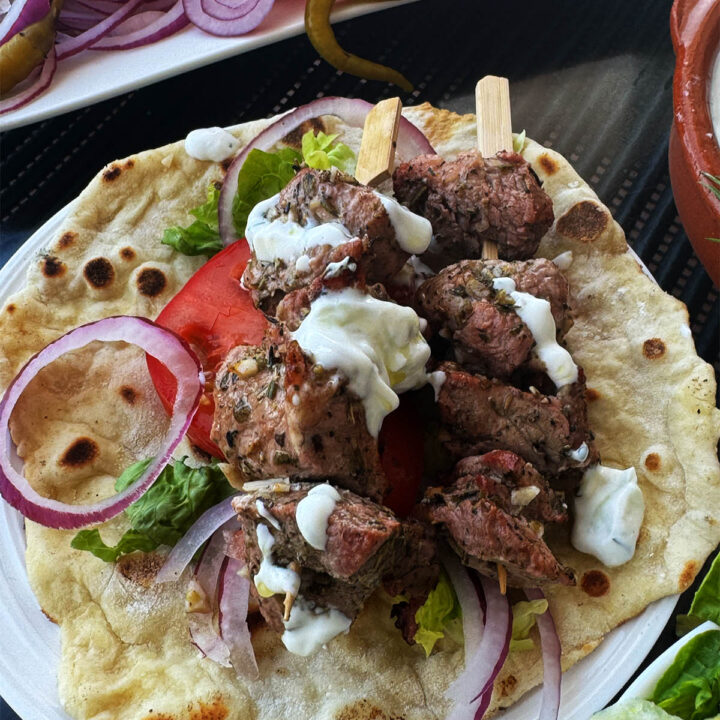 Pork souvlaki on a pita with tzatziki and salad vegetables.