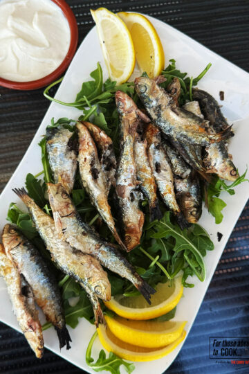 Grilled sardines with salt served on a plate with lemon wedges.