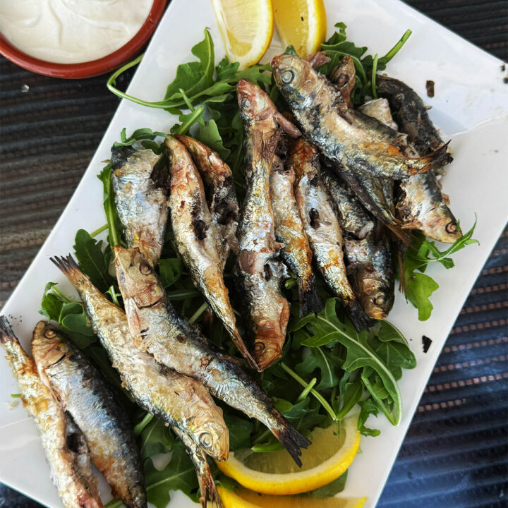 Grilled sardines with salt served on a plate with lemon wedges.