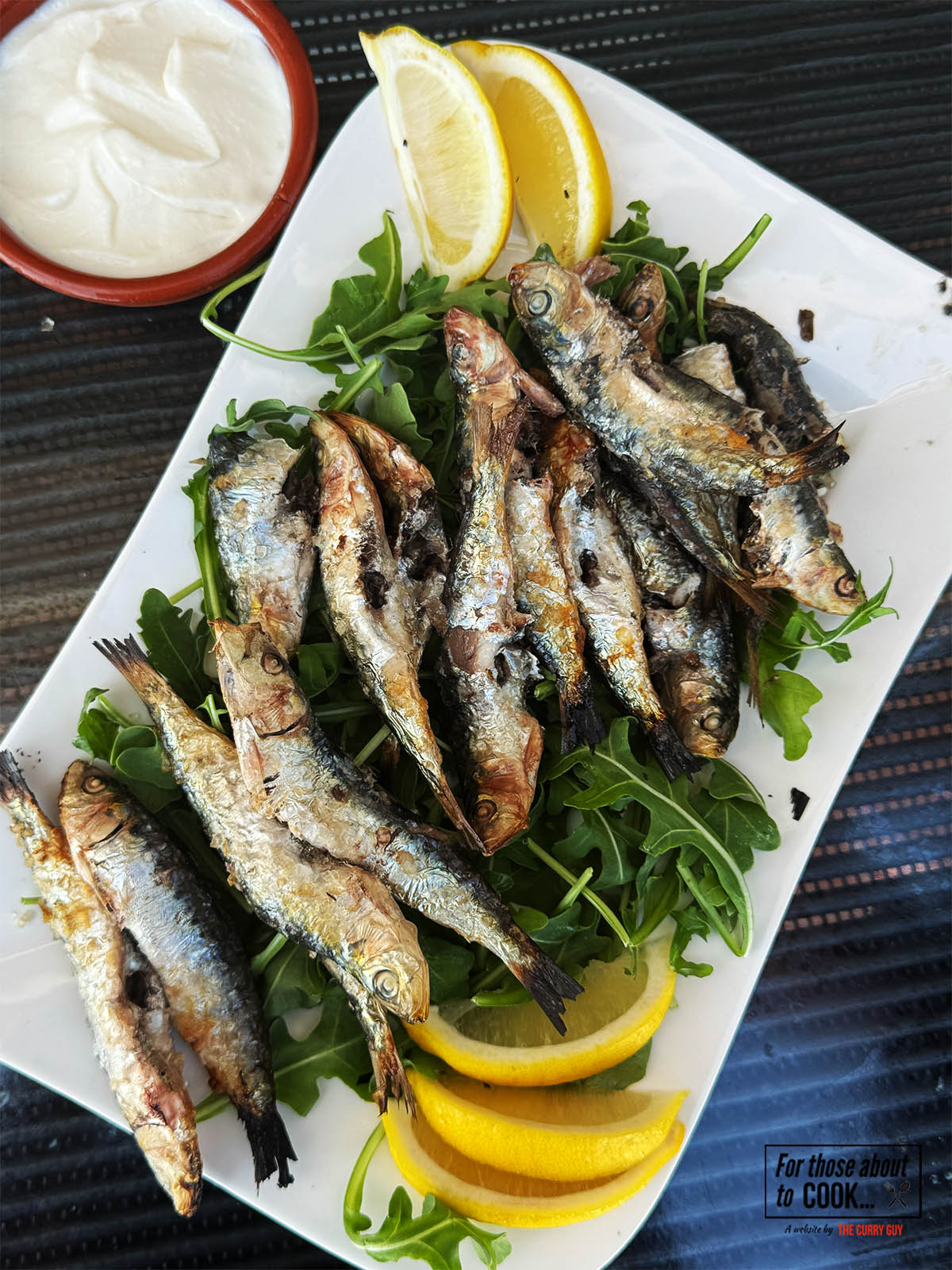 Grilled sardines with salt served on a plate with lemon wedges.