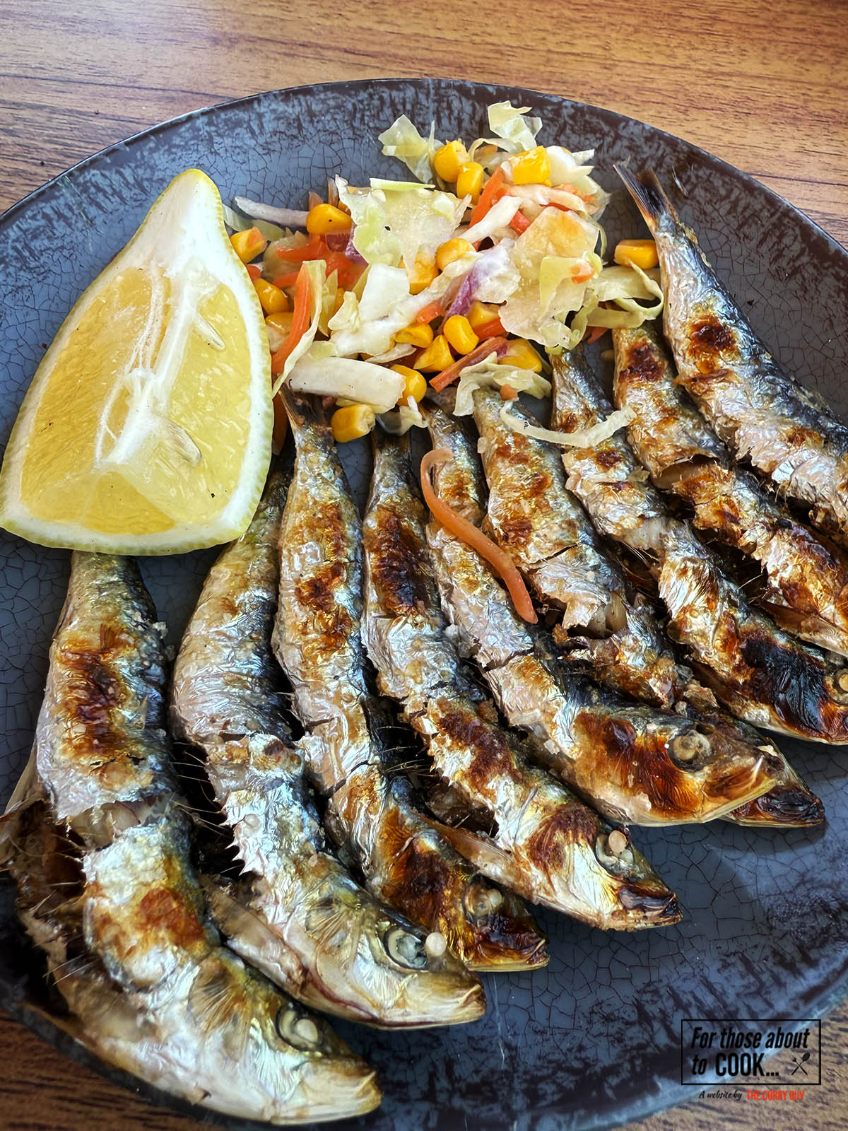 Grilled sardines with salt served on a plate with salad and lemon wedges.