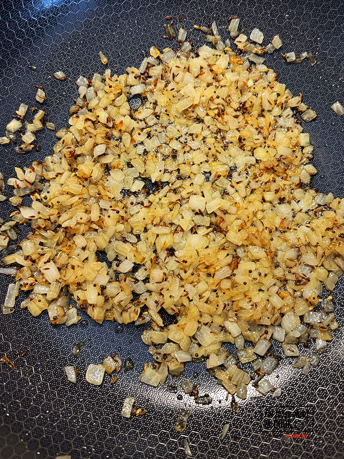 Chopped onions browning in a pan with oil and toasted seeds