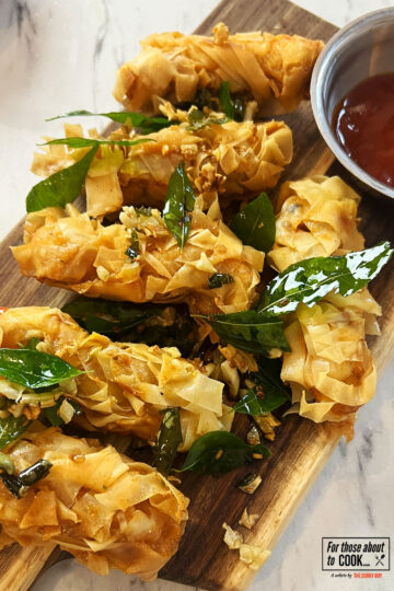Crispy threaded chicken served on a board and topped with garlic and curry leaves