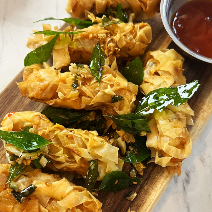 Crispy threaded chicken served on a board and topped with garlic and curry leaves