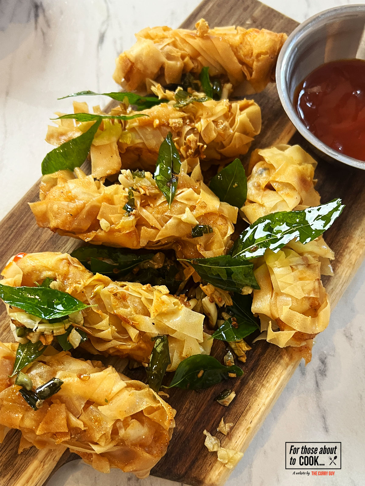 Crispy threaded chicken served on a board and topped with garlic and curry leaves