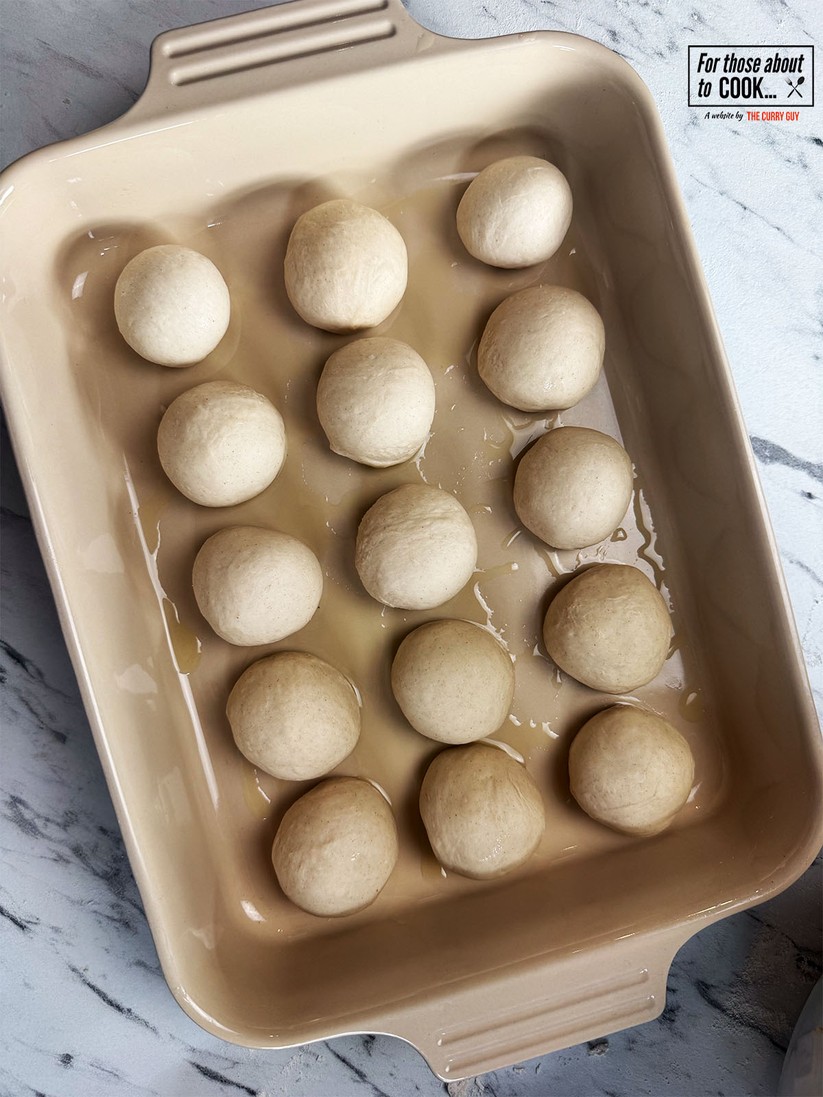 Dough balls spread out in an oiled oven proof dish 
