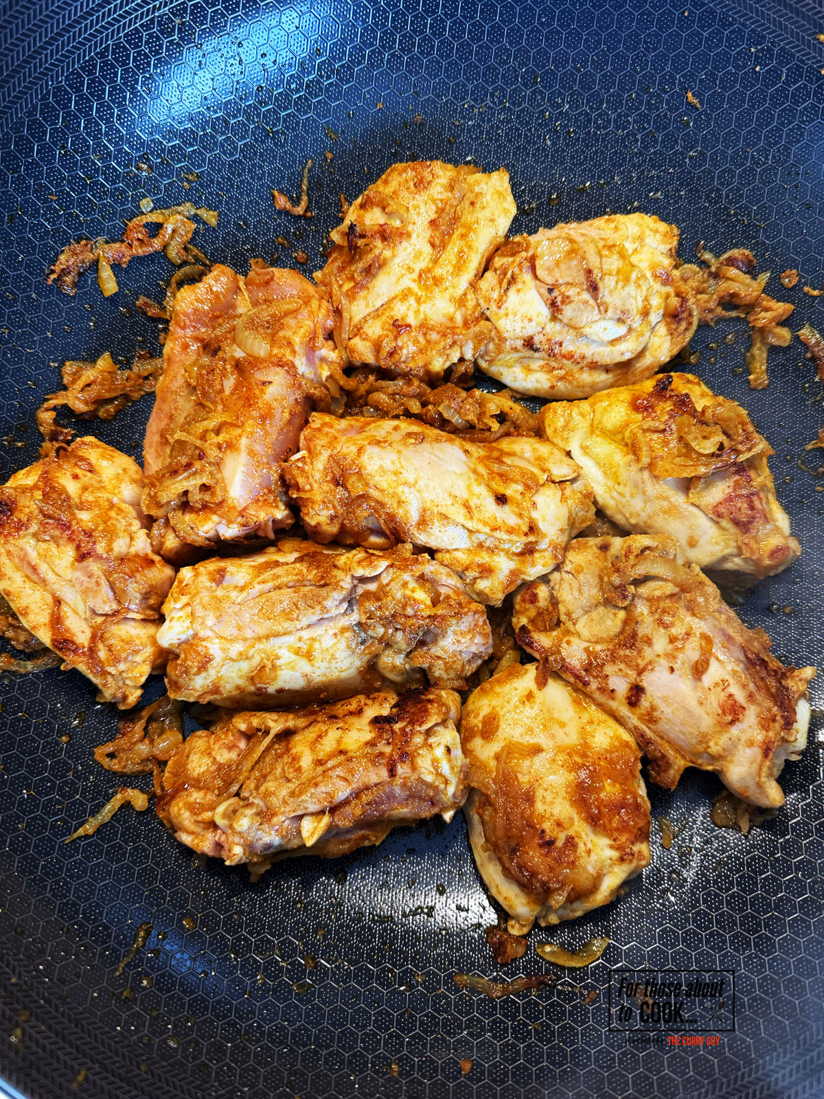 Chicken browning in the pan with onions and spices