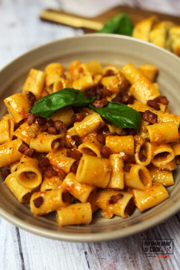 Pasta alla zozzona served in a bowl topped with pancetta and basil