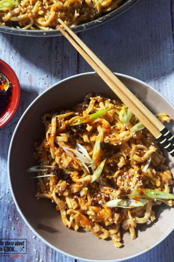 Peanut butter noodles served in a bowl topped with spring onion and sesame seeds