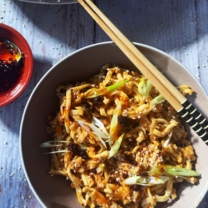 Peanut butter noodles served in a bowl topped with spring onion and sesame seeds