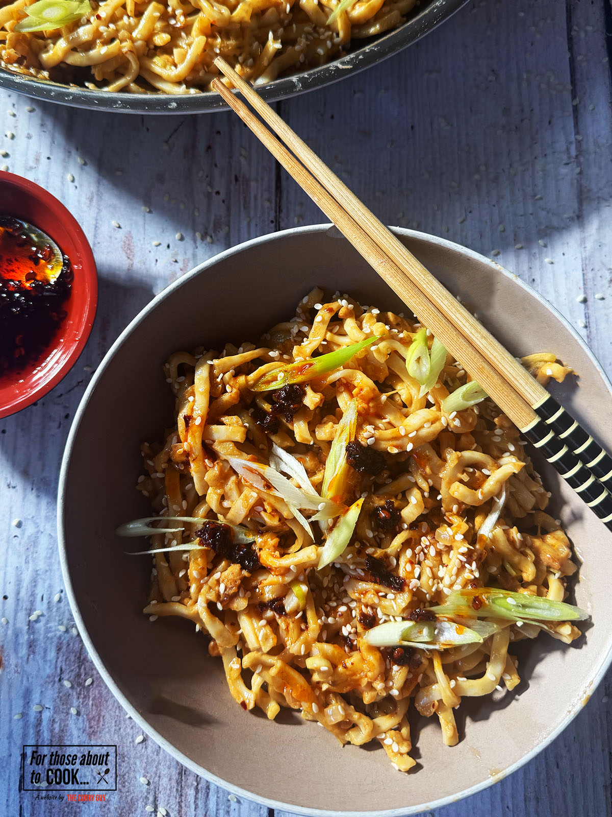 Peanut butter noodles served in a bowl topped with spring onion and sesame seeds